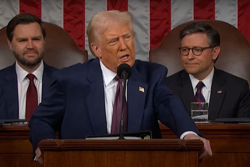 The President of the United States signs documents against the backdrop of a flag